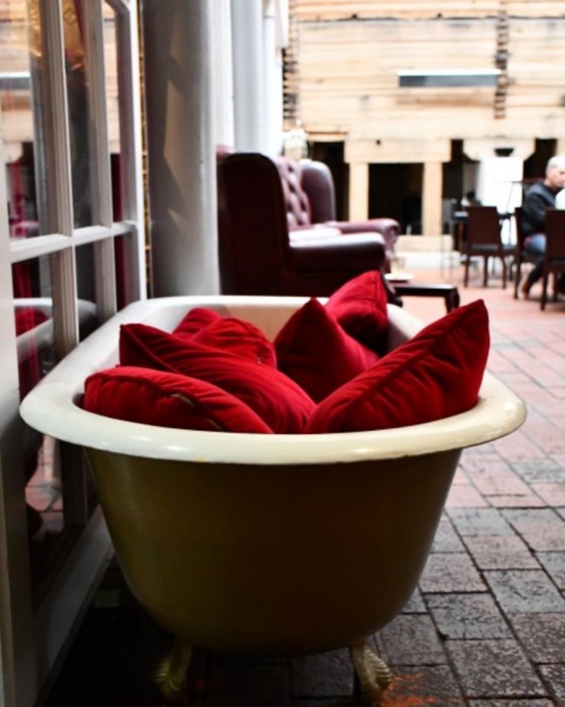A gold bath with red cushions inside sitting in an enclosed area.
